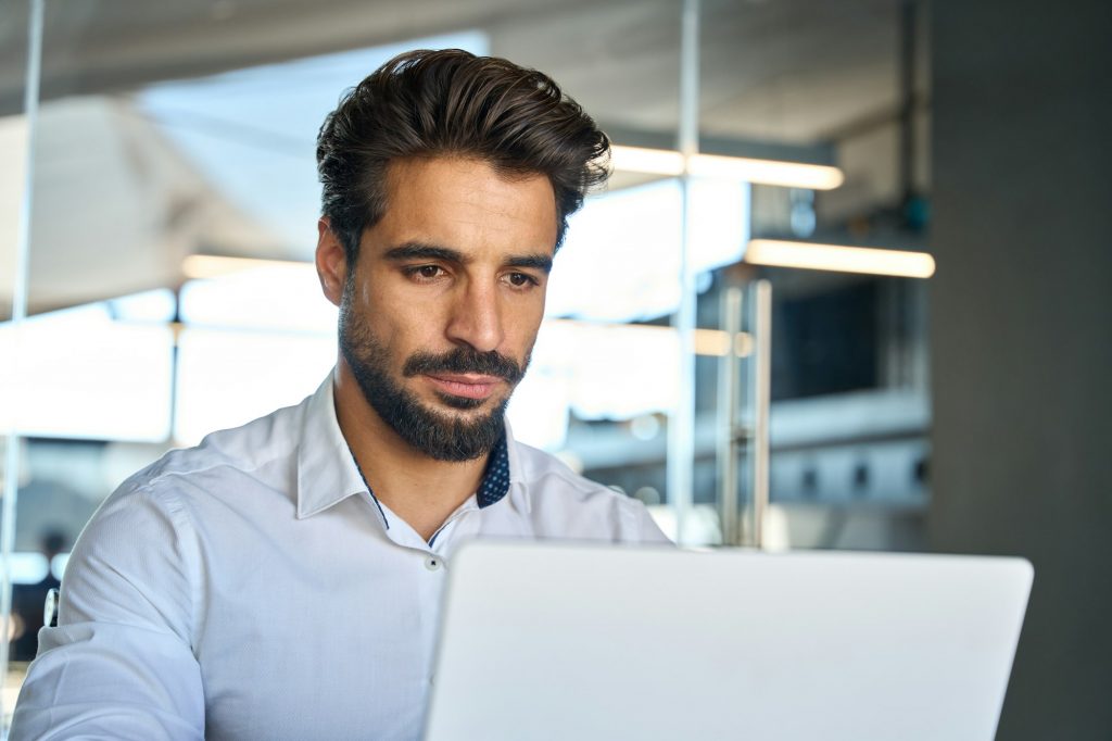 Busy young Latin business man looking at laptop using computer at work.